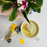 A pack of lemon turmeric energy balls with a pukka lemon & ginger cup of herbal tea next to a bouquet of flowers