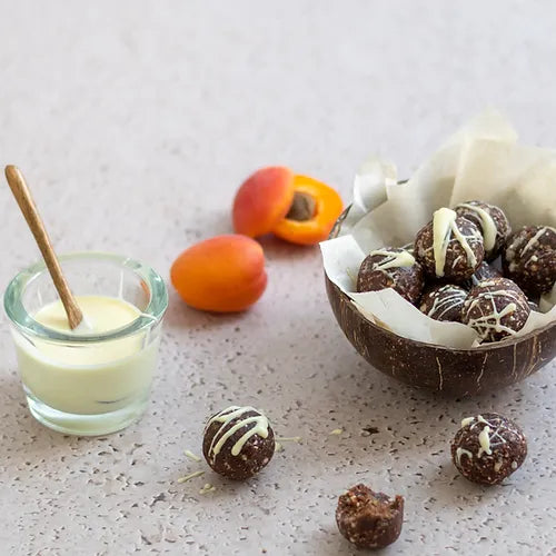 A bowl of Apricot & Hazelnut Cacao Energy Balls with fresh apricots at the side